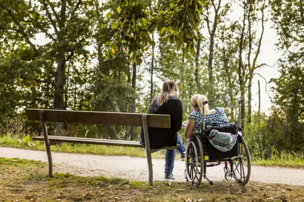 Disabled woman in wheelchair with assistant in park